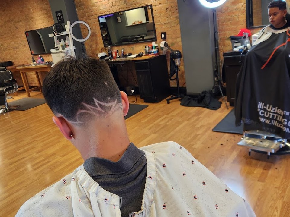 A fade with a shaved design on the back of the head, inside the shop with brick walls and ring lights.